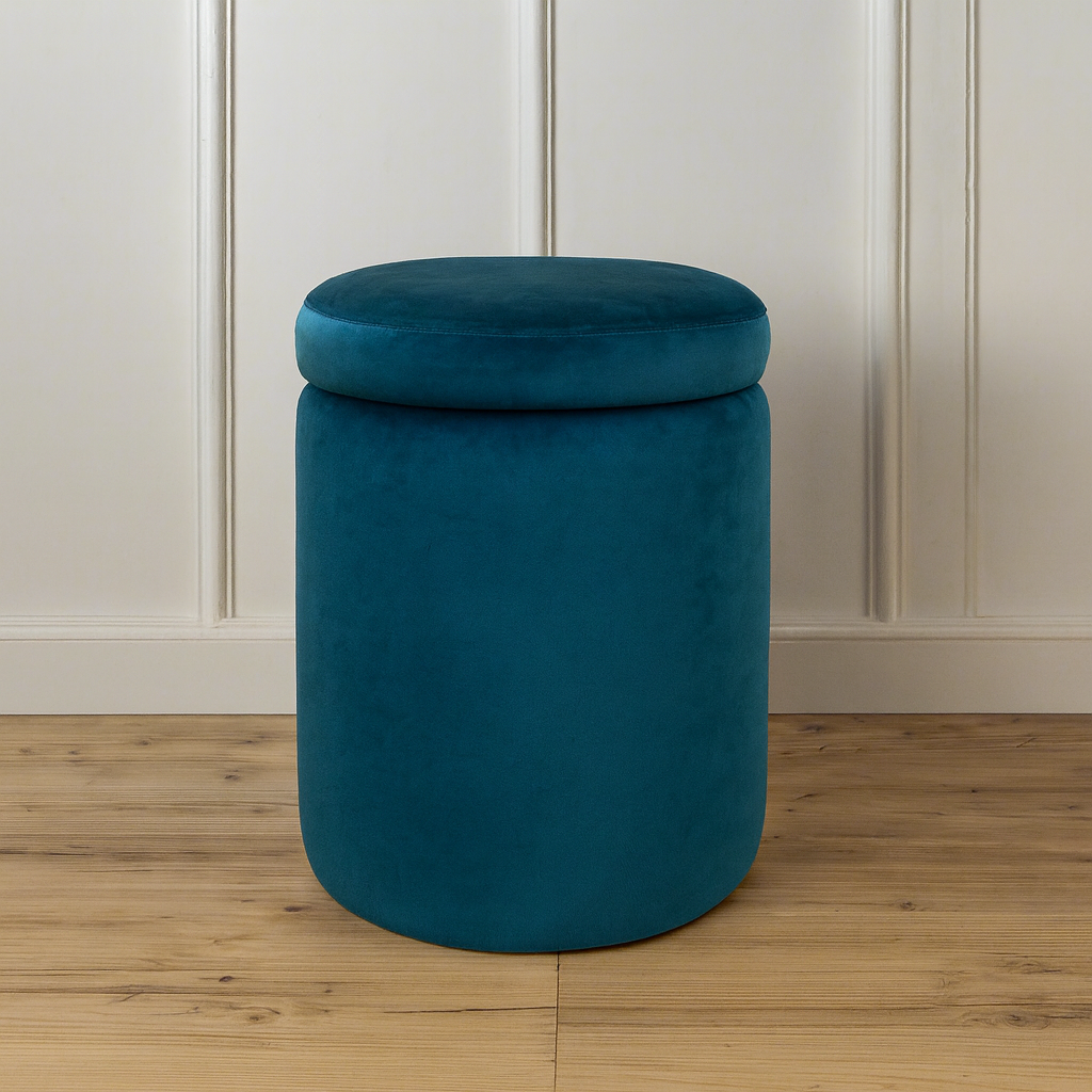 Teal cylindrical ottoman with a lid on a wooden floor against a white paneled wall.