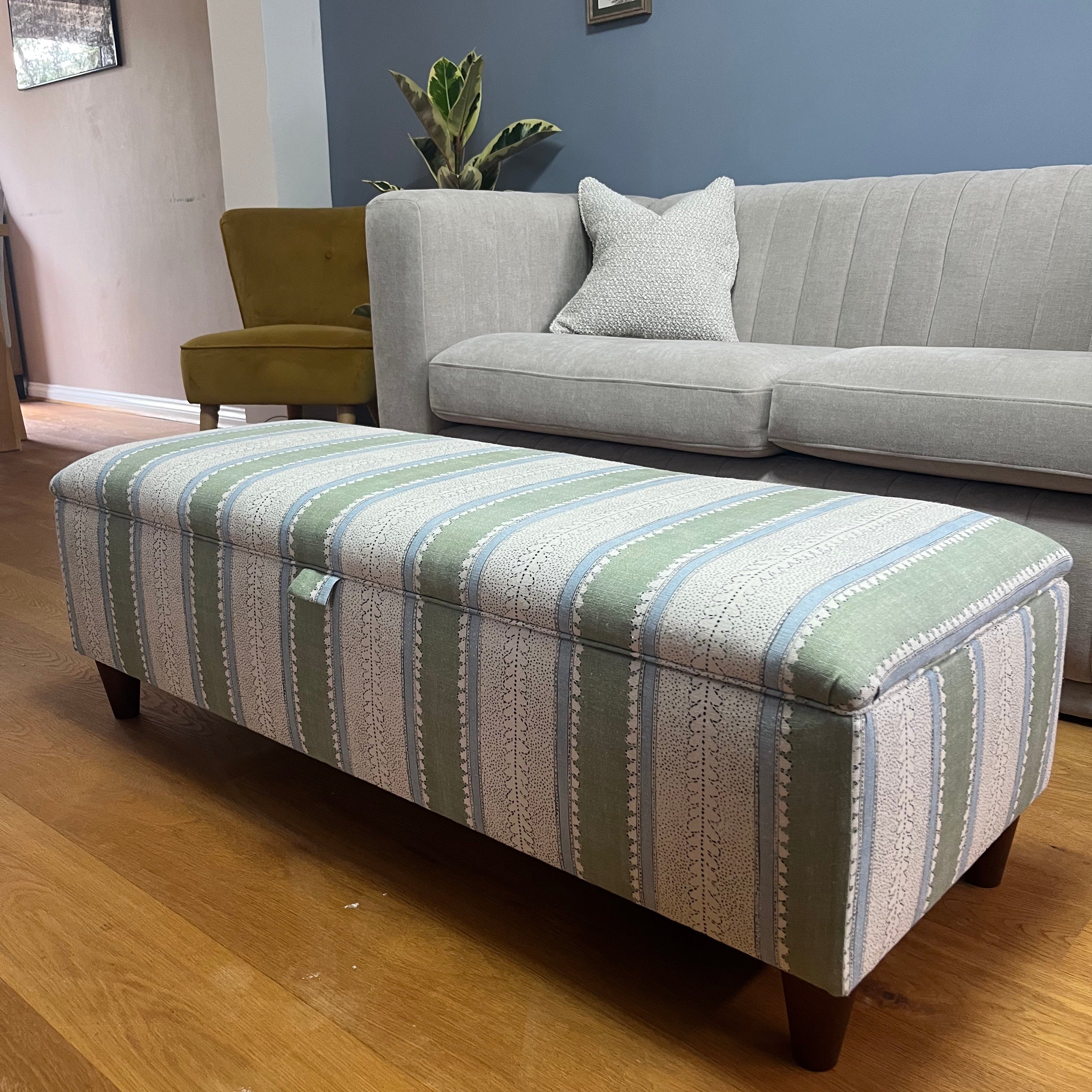 Grey sofa with striped ottoman against a blue wall with a yellow accent chair