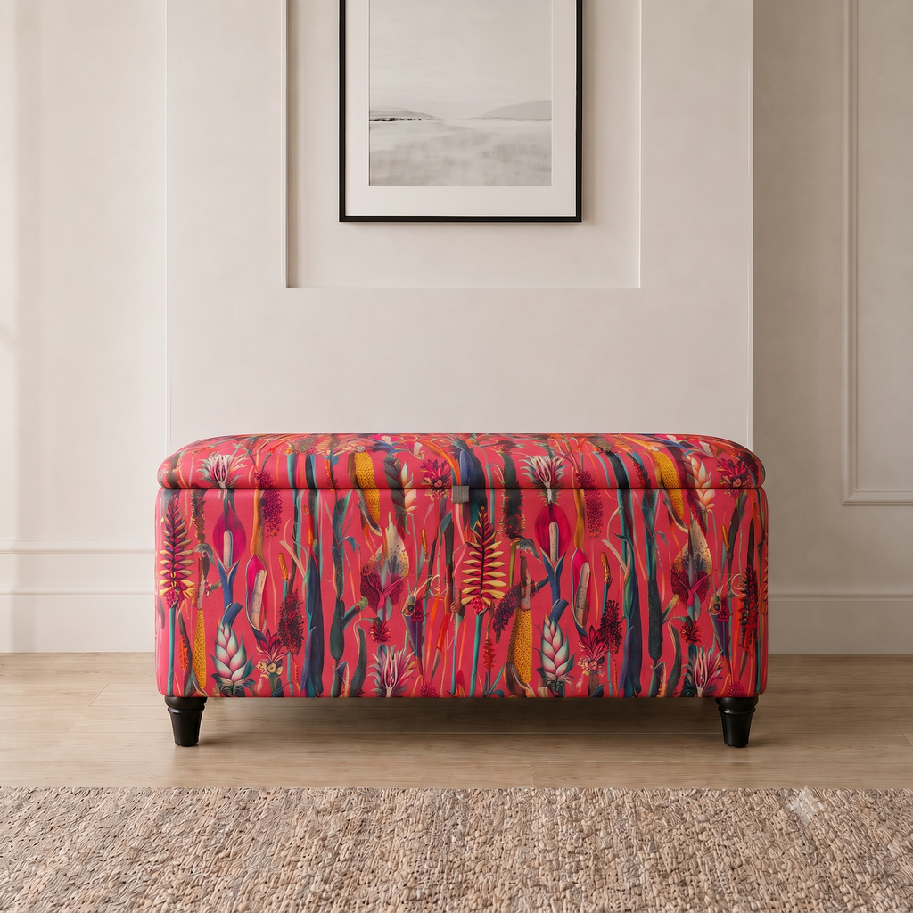 A rectangular upholstered storage bench with a dark navy floral and bird pattern, standing on a light wood floor in front of a cream paneled wall.