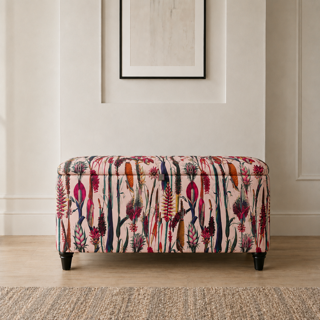 A rectangular storage bench with a floral and botanical patterned upholstery in pink, red, purple, and green, supported by four dark legs, set against a neutral beige wall with a framed print.