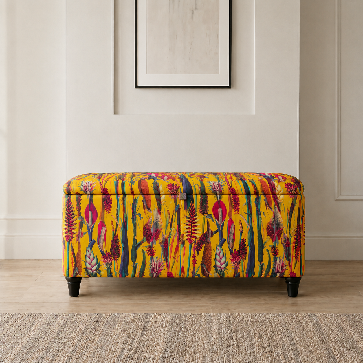A rectangular upholstered bench with a bright yellow base and a multicolored botanical pattern, standing on black legs in a styled interior setting.