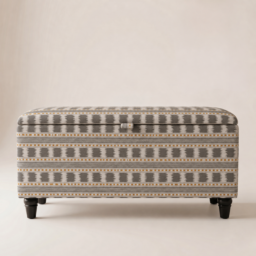 An upholstered storage ottoman with a geometric pattern in gray, beige, and mustard yellow, supported by dark wooden legs.