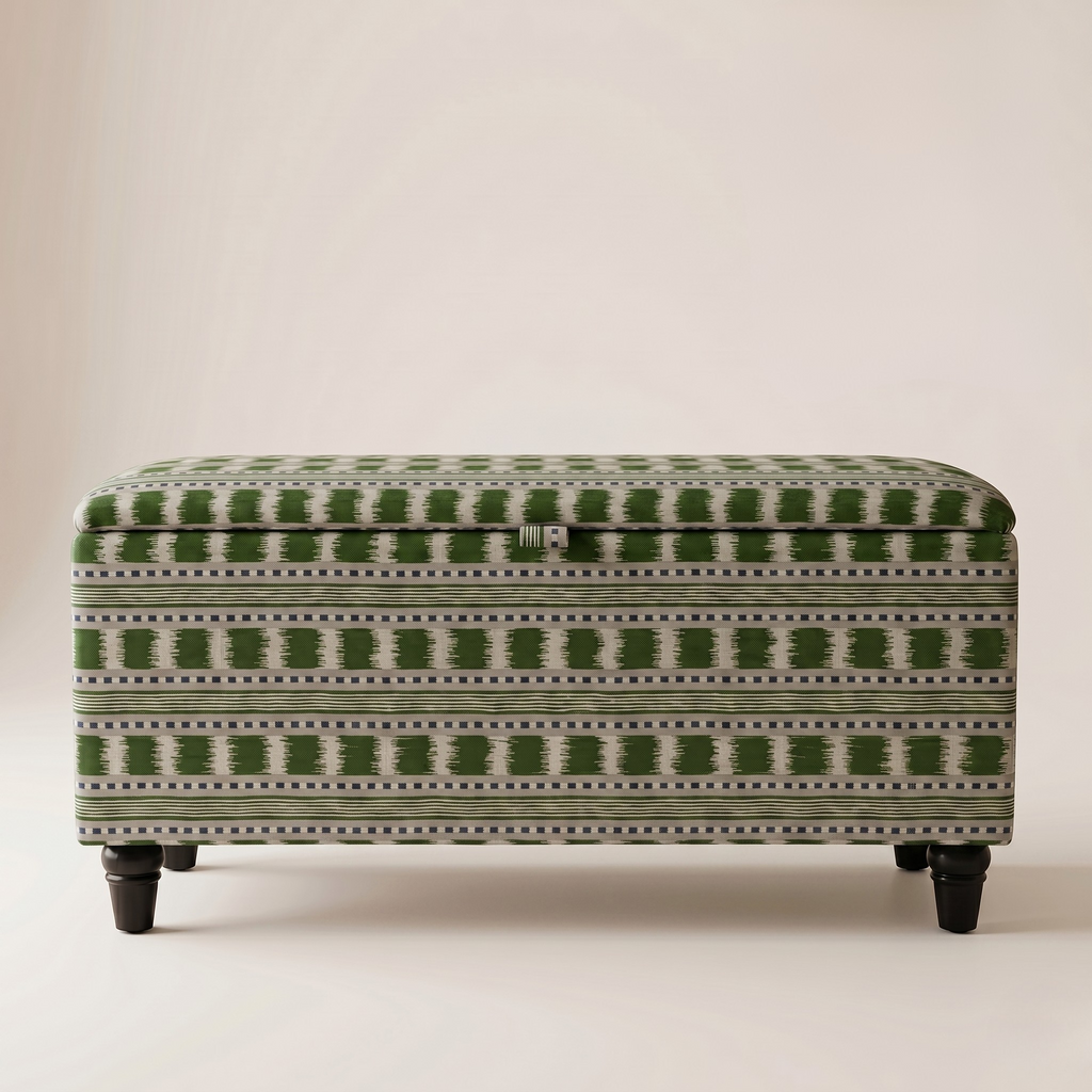 An upholstered storage bench or ottoman with a green and off-white geometric pattern, supported by four dark legs, photographed against a neutral beige background.
