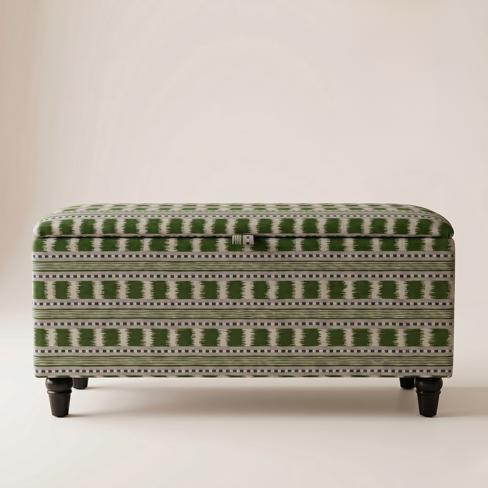 An upholstered storage bench or ottoman with a green and off-white geometric pattern, supported by four dark legs, photographed against a neutral beige background.