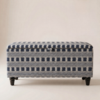 An upholstered storage bench with a navy blue and off-white geometric pattern, featuring dark wooden legs, set against a plain beige background.