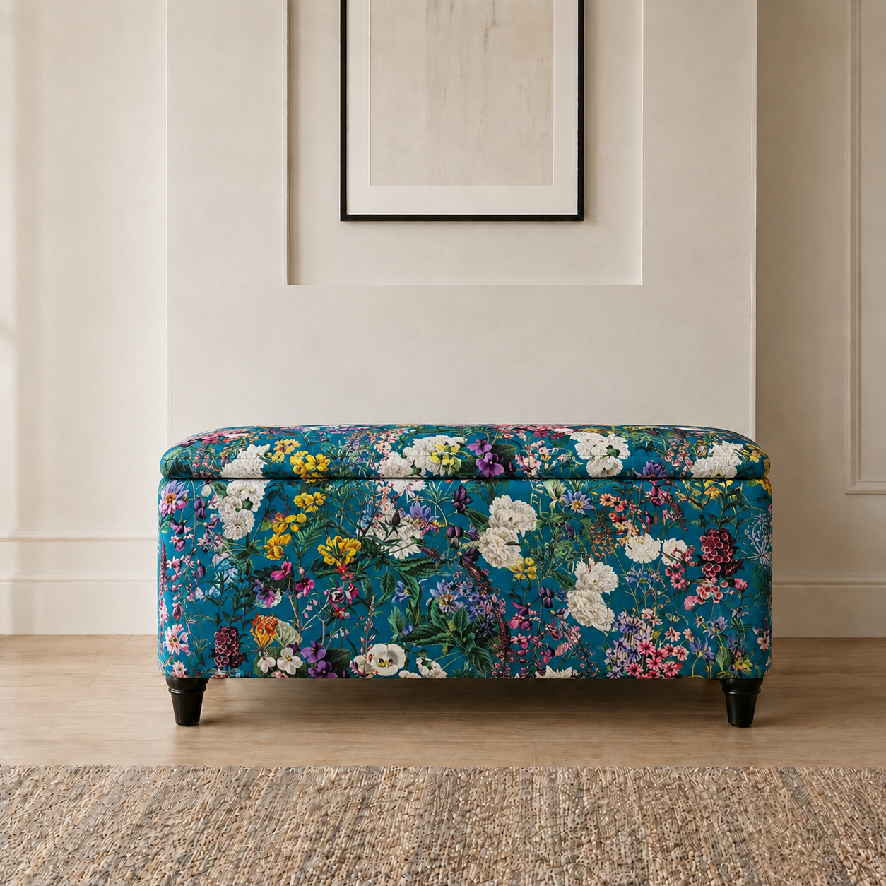 A rectangular upholstered storage bench with a vibrant multicolor floral pattern on a teal background, featuring dark wooden legs, set in a styled room with a light wood floor and a neutral wall.