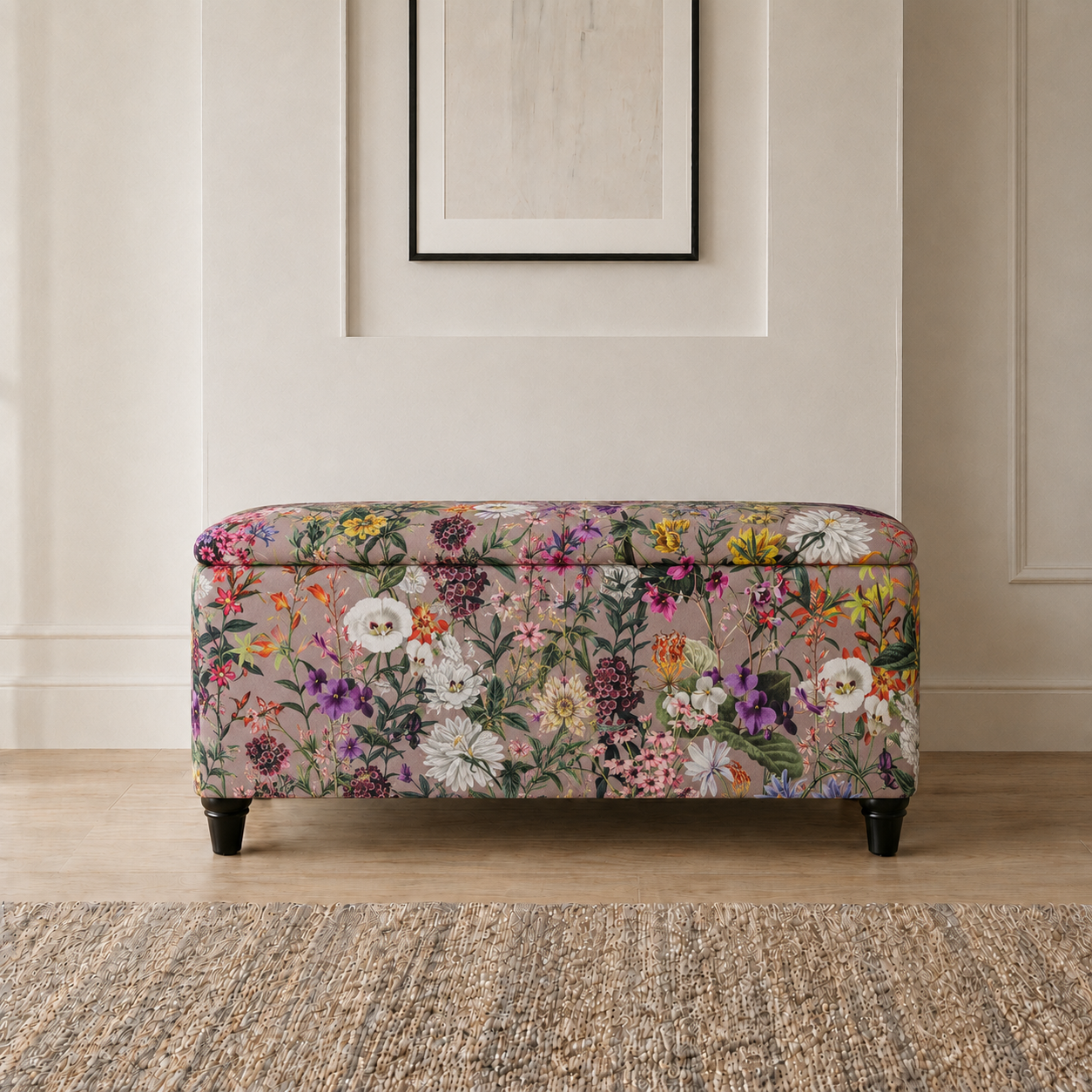 A floral storage bench with a floral patterned fabric upholstery, dark wooden legs, and a hinged lid, set against a neutral beige wall with a framed picture above.