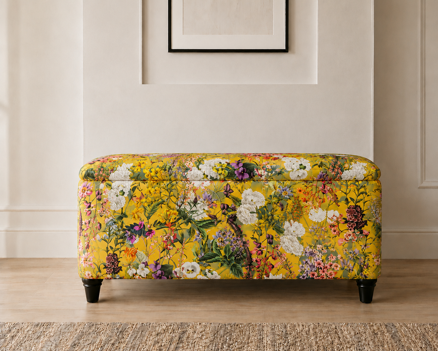 A rectangular upholstered bench with a vibrant yellow floral pattern, supported by four black legs, set against a neutral beige wall and light wood floor.