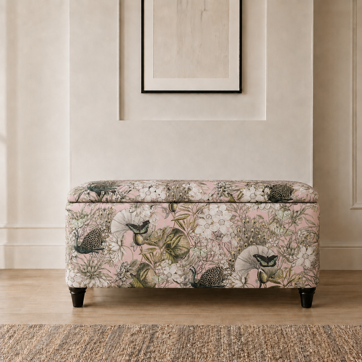A rectangular upholstered storage bench with a floral and bird pattern in soft pink, beige, and green, set against a neutral cream wall with a framed print above.