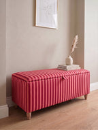 A rectangular storage bench with a red and pink Sanderson regency vertically striped fabric upholstery and light wood legs, styled in a home entryway setting with a vase and books on top.