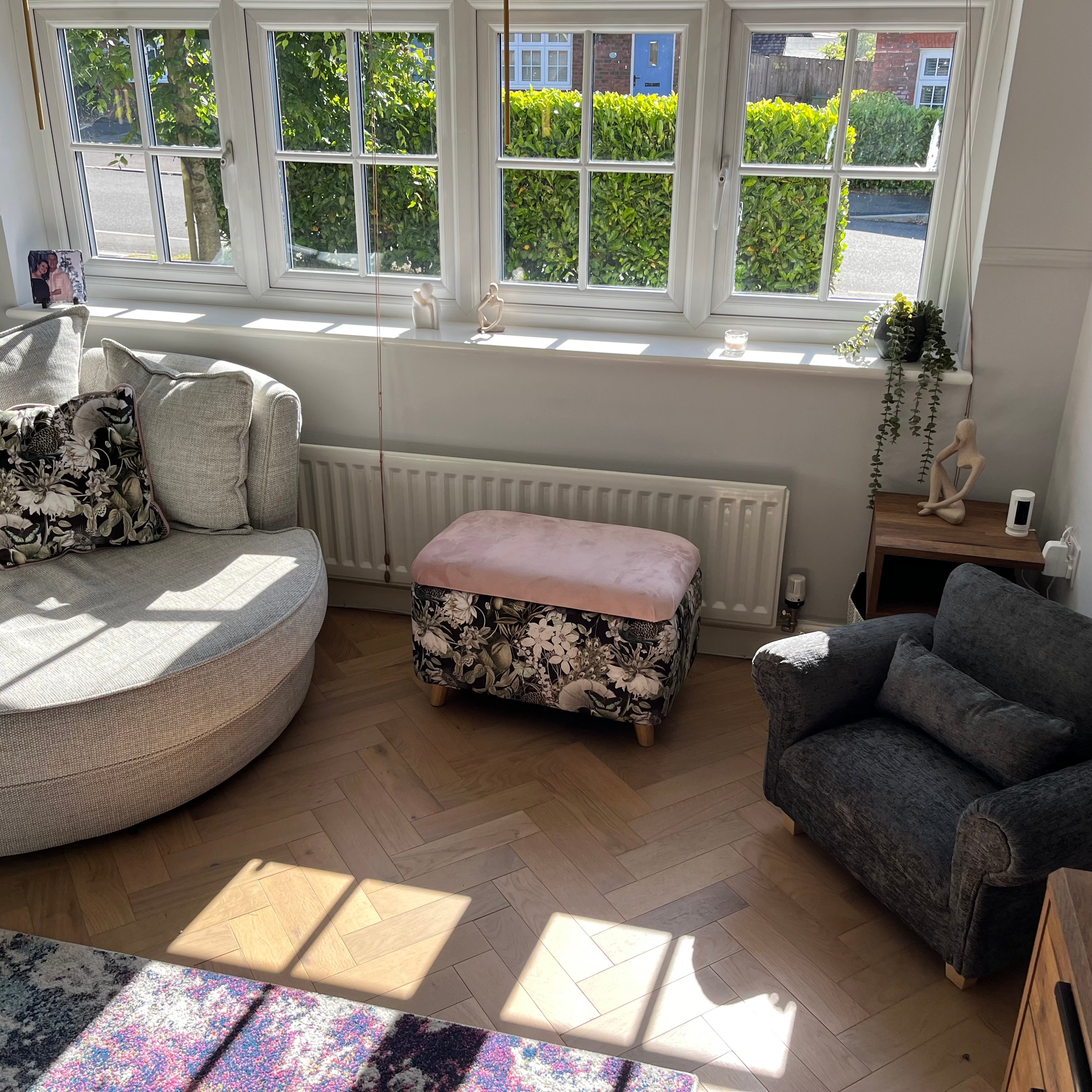 living room with parquet flooring and a black floral ottoman footstool with a small miniature dog sofa in charcoal.
