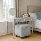Dresser with mirror and gray ottoman in a bedroom setting