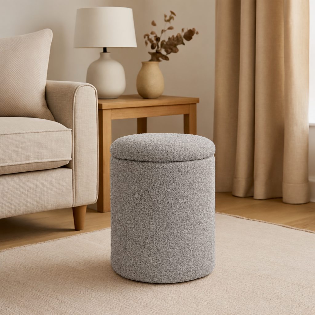 Gray ottoman in a living room setting with a beige sofa, lamp, and curtains.