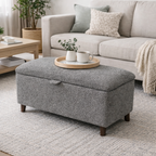 Gray storage ottoman in a living room with a coffee table and couch.
