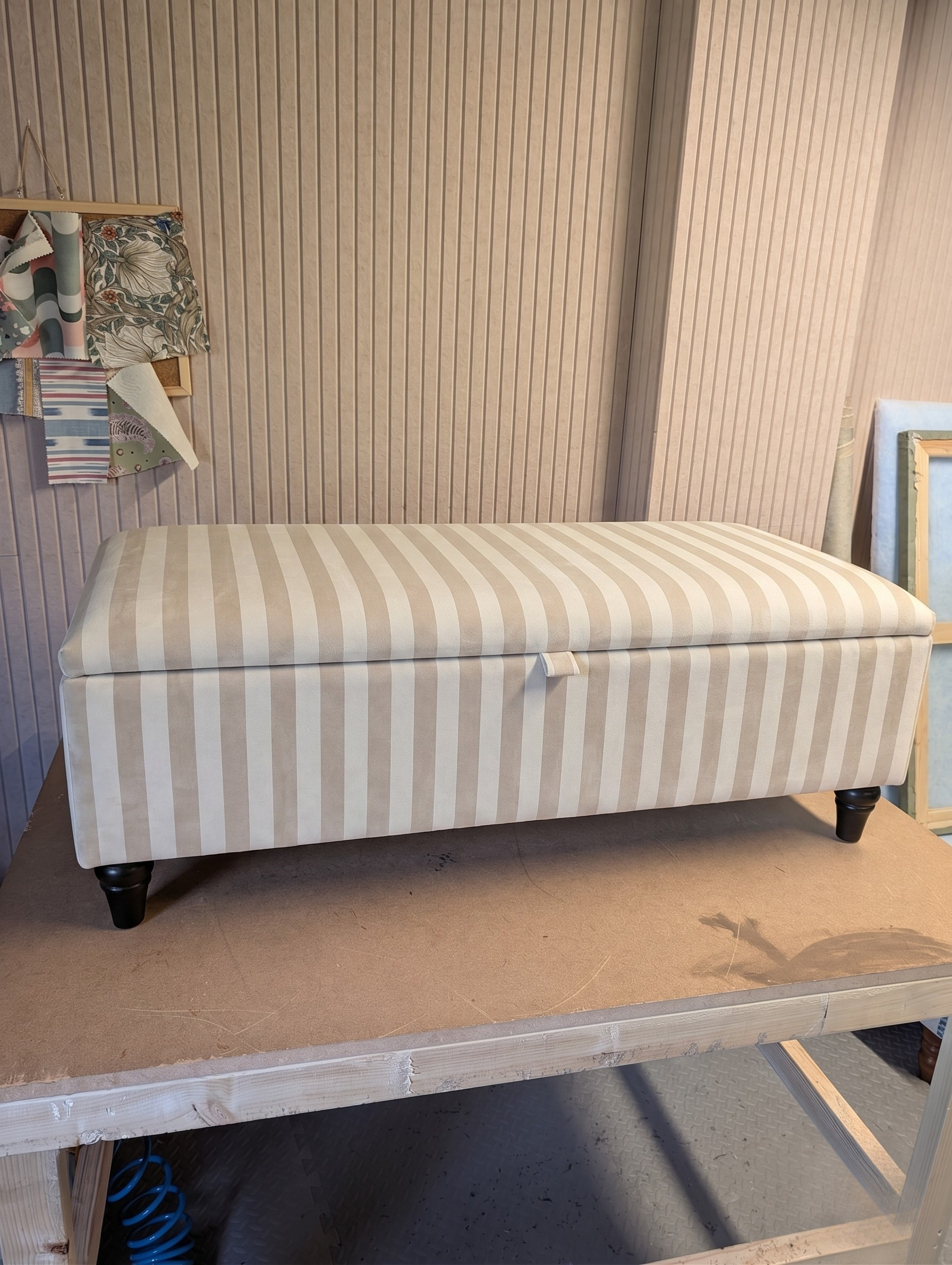 Workshop image of a striped storage ottoman on a wooden work bench