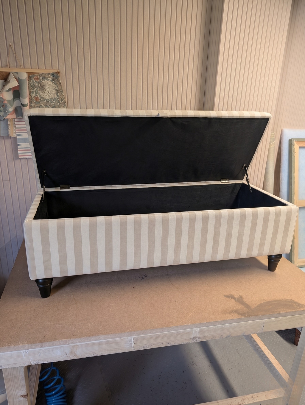 Open storage ottoman with antique coloured stripes on a workbench.