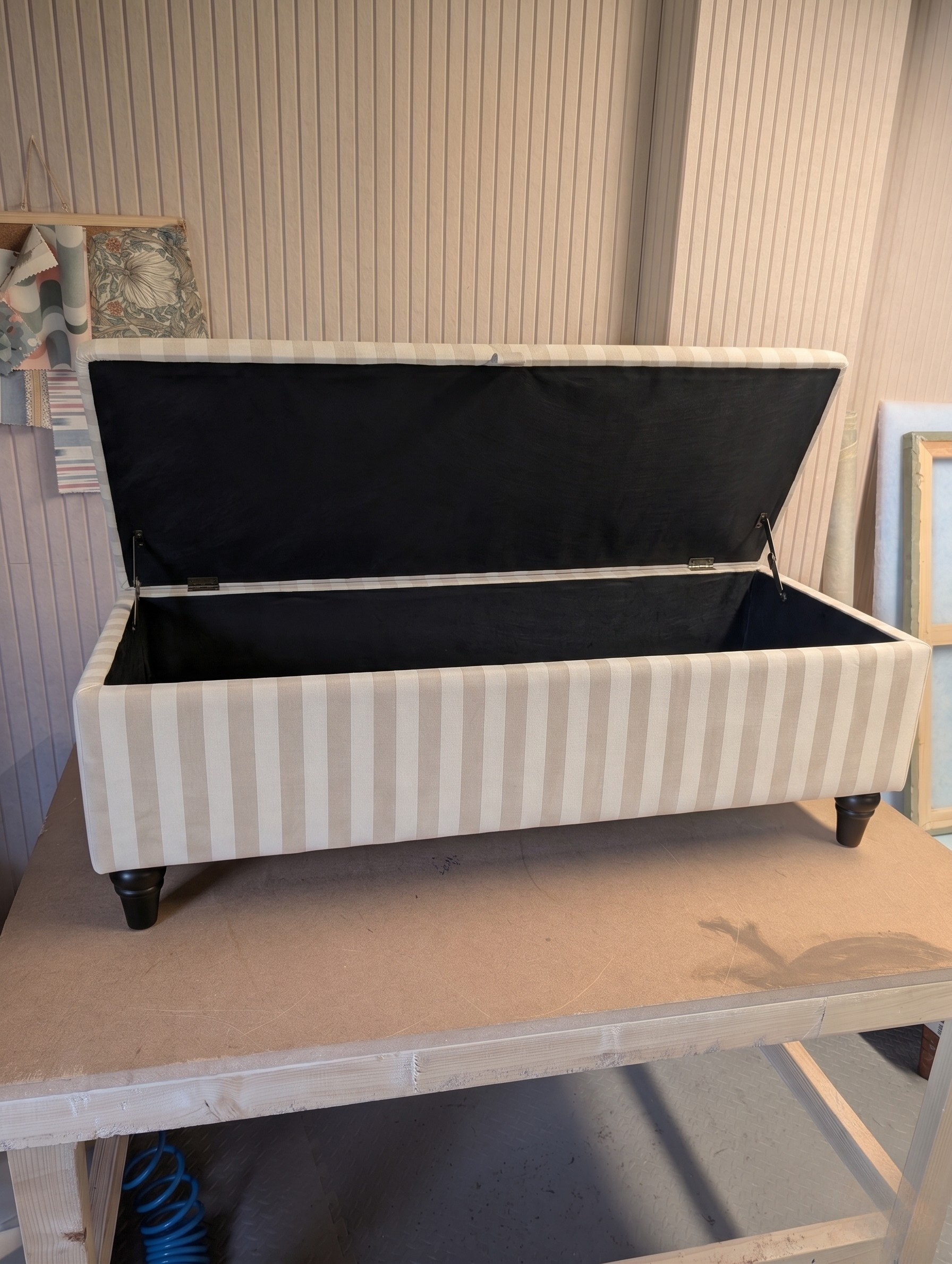 Open storage ottoman with antique coloured stripes on a workbench.
