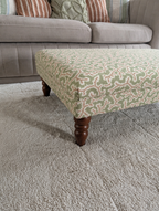 Handmade green and cream upholstered footstool with turned wooden legs, styled as a living room coffee table ottoman in front of a neutral sofa.