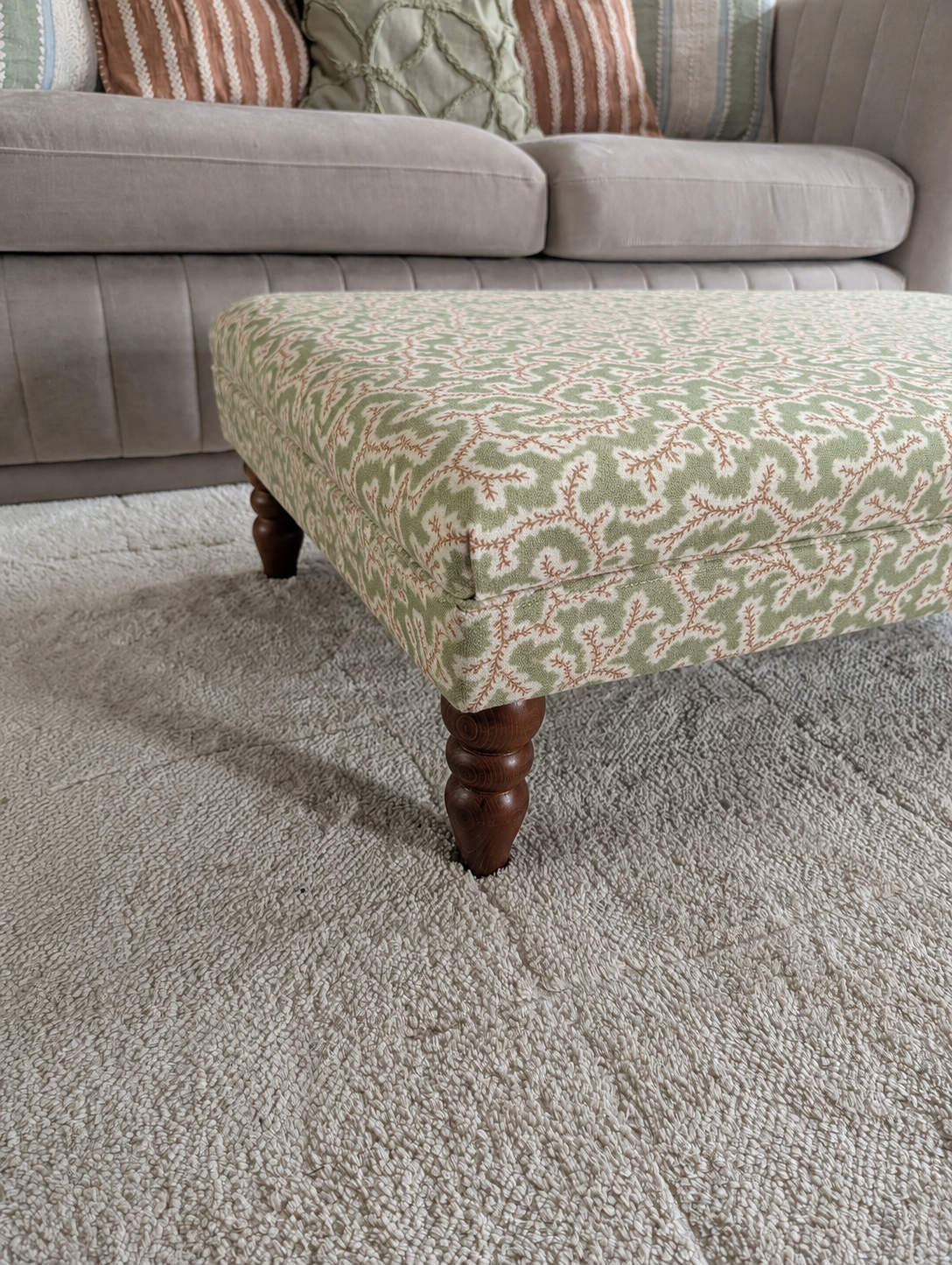 Handmade green and cream upholstered footstool with turned wooden legs, styled as a living room coffee table ottoman in front of a neutral sofa.