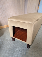 Beige ottoman with a wooden interior on a textured floor.