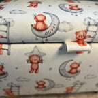 personalised childrens fabric with white background and brown teddy bears on. The bears are hanging off of moons and stars which have 'Oliver' written on them and can be personalised to a childs name.