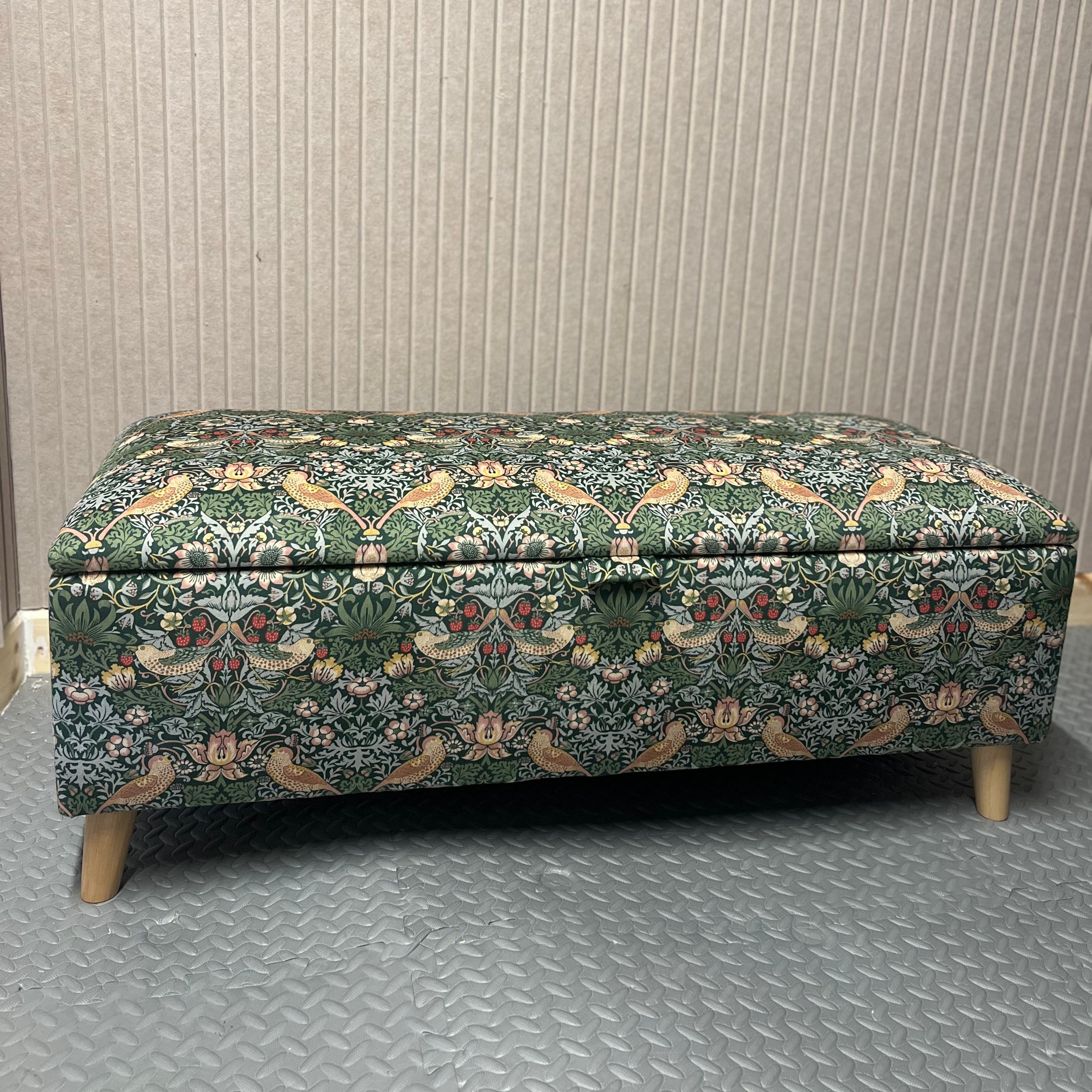 Forest strawberry Thief storage ottoman with a lid on a textured floor and wall background