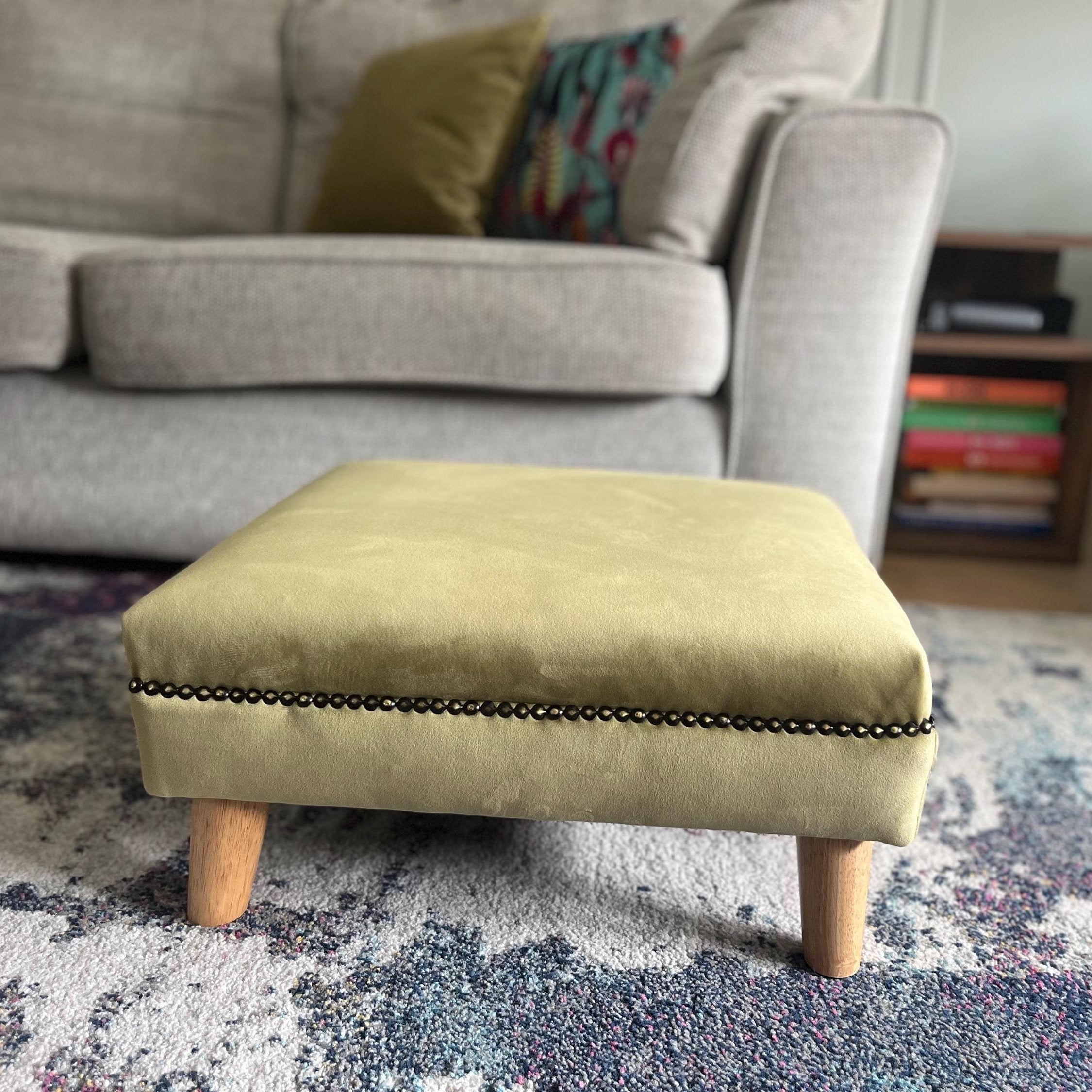 Low footstool in olive green plush velvet with wooden feet
