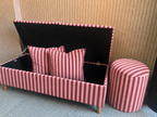 Pink striped storage bench with cushions against a wooden wall.