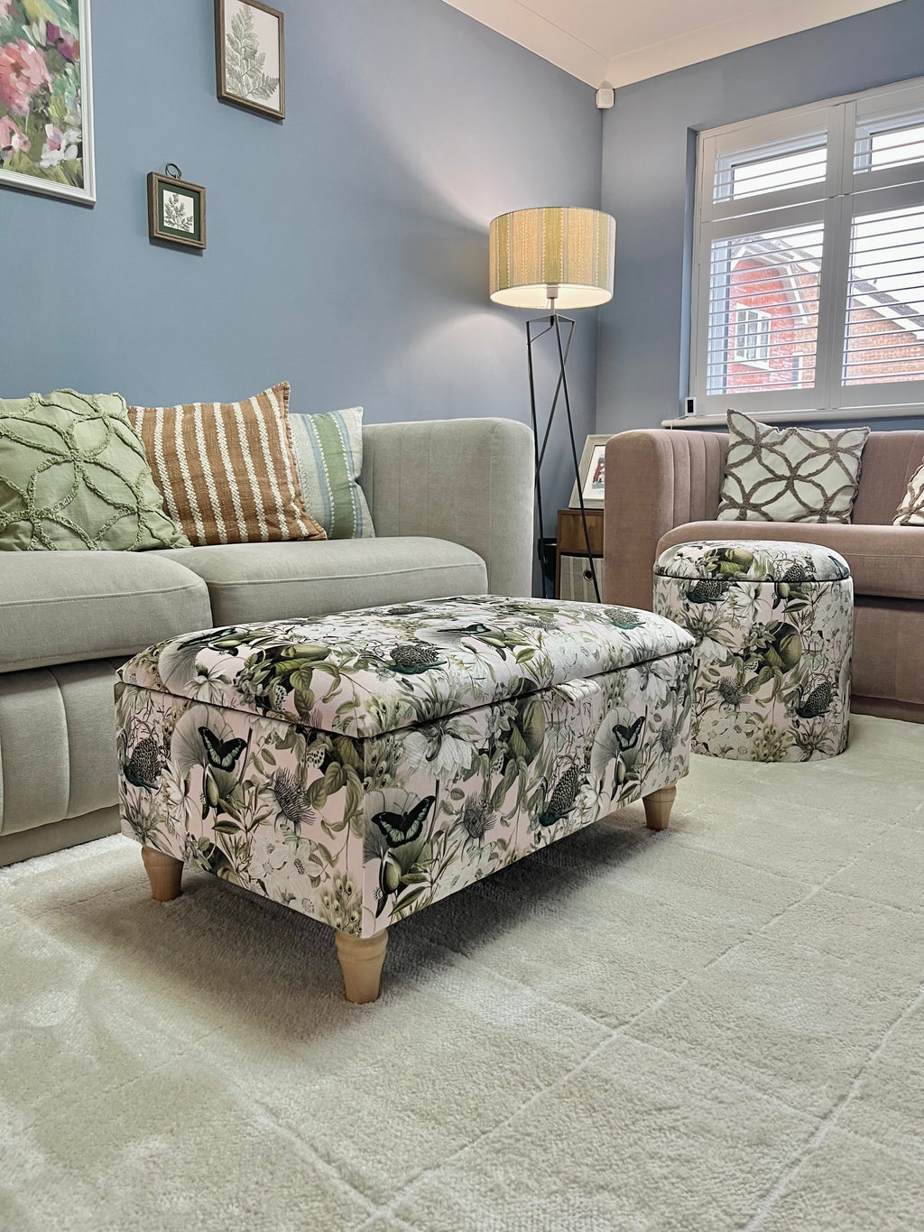 Living room with floral-patterned butterfly ottoman, gray sofa, and dusty pink armchair.