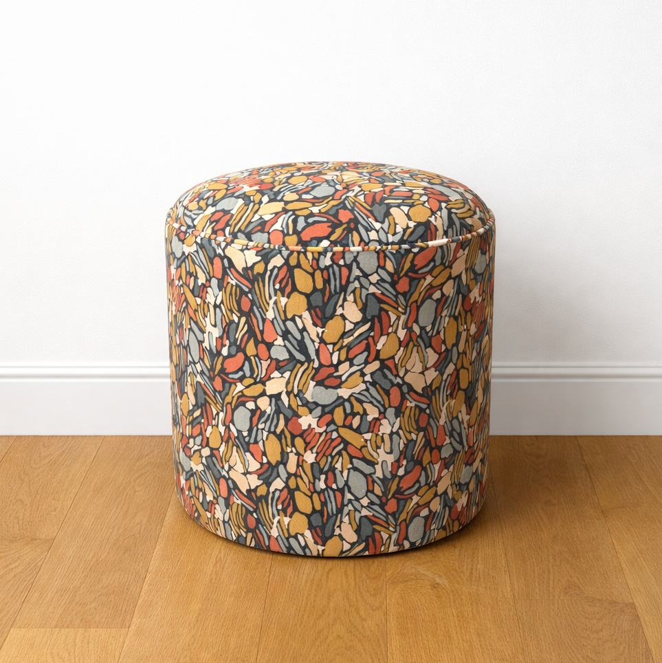 Multicolored patterned ottoman on a wooden floor with a white wall background