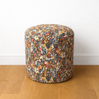 Multicolored patterned ottoman on a wooden floor with a white wall background