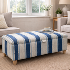 Blue and white striped ottoman in a living room setting with a window and furniture in the background.