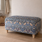 Blue strawberry thief patterned ottoman on a wooden floor with a neutral rug and wall in the background