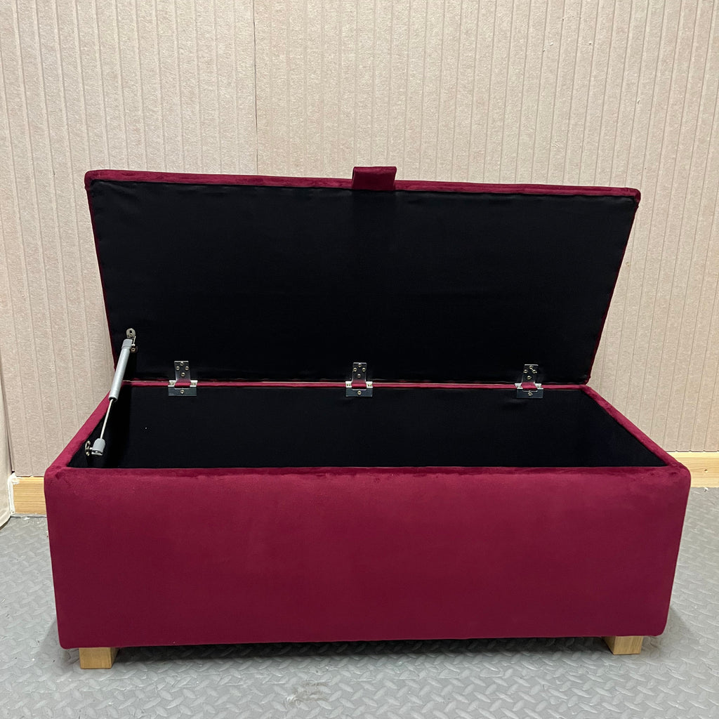 Maroon ottoman with open lid against a textured wall.