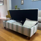 Green, blue and white striped ottoman with walnut legs, open with blankets and cushions inside.