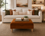 A styled living room scene featuring a cream upholstered sofa with olive green, rust brown, and cream striped throw pillows, paired with a rust brown ottoman in the foreground on a woven rug.