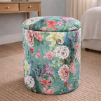 Floral-patterned ottoman in a room with a mirror and flowers on a table.