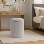 Gray textured ottoman in a bedroom setting with a bed, desk, and wall lights.