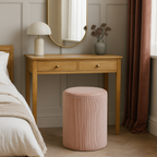 Wooden vanity table with round mirror, lamp, and vase in a bedroom setting. Pink stripe dressing stool on a wooden floor.