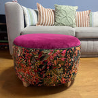Decorative ottoman with floral pattern next to a sofa with striped cushions on a wooden floor.