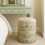 Decorative beige ottoman with floral strawberry thief pattern in front of a green vanity with mirror