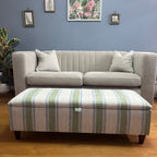 Grey sectional sofa with stripes storage footstool against a blue wall with framed pictures.