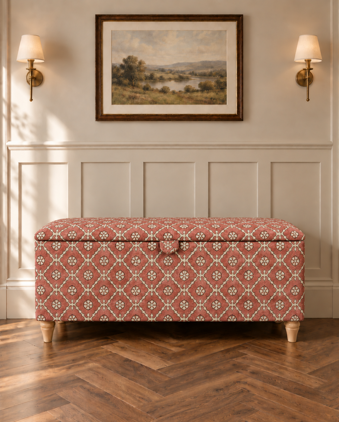 A storage bench with a patterned dusty rose and cream fabric, styled in a traditional room setting with a wooden herringbone floor, white wainscoting, wall sconces, and a framed landscape painting.