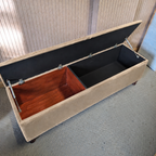 Beige storage bench with open lid revealing a partial wooden interior, against a neutral background.
