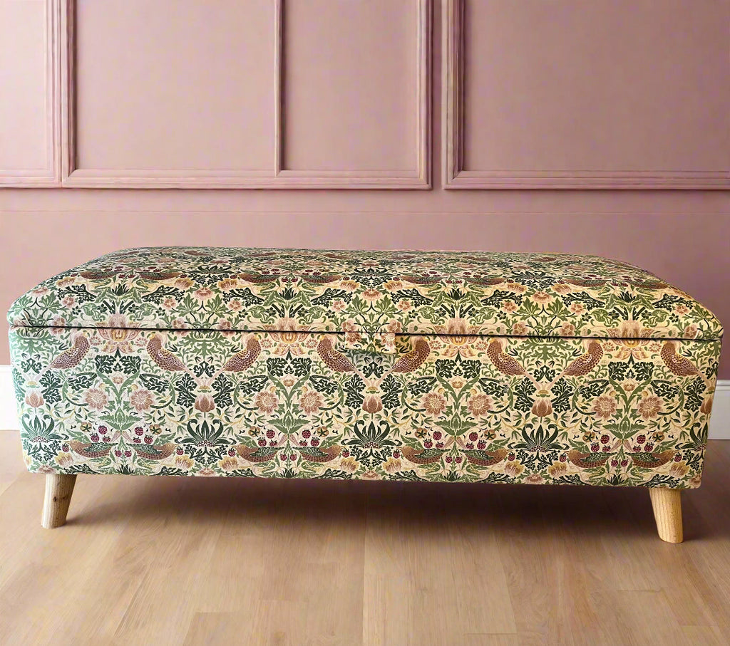 A rectangular storage ottoman upholstered in William Morris velvet with angled feet, featuring a floral pattern in a mix of gold, black, and green colors.