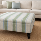 Striped ottoman in front of a beige sofa with decorative pillows.