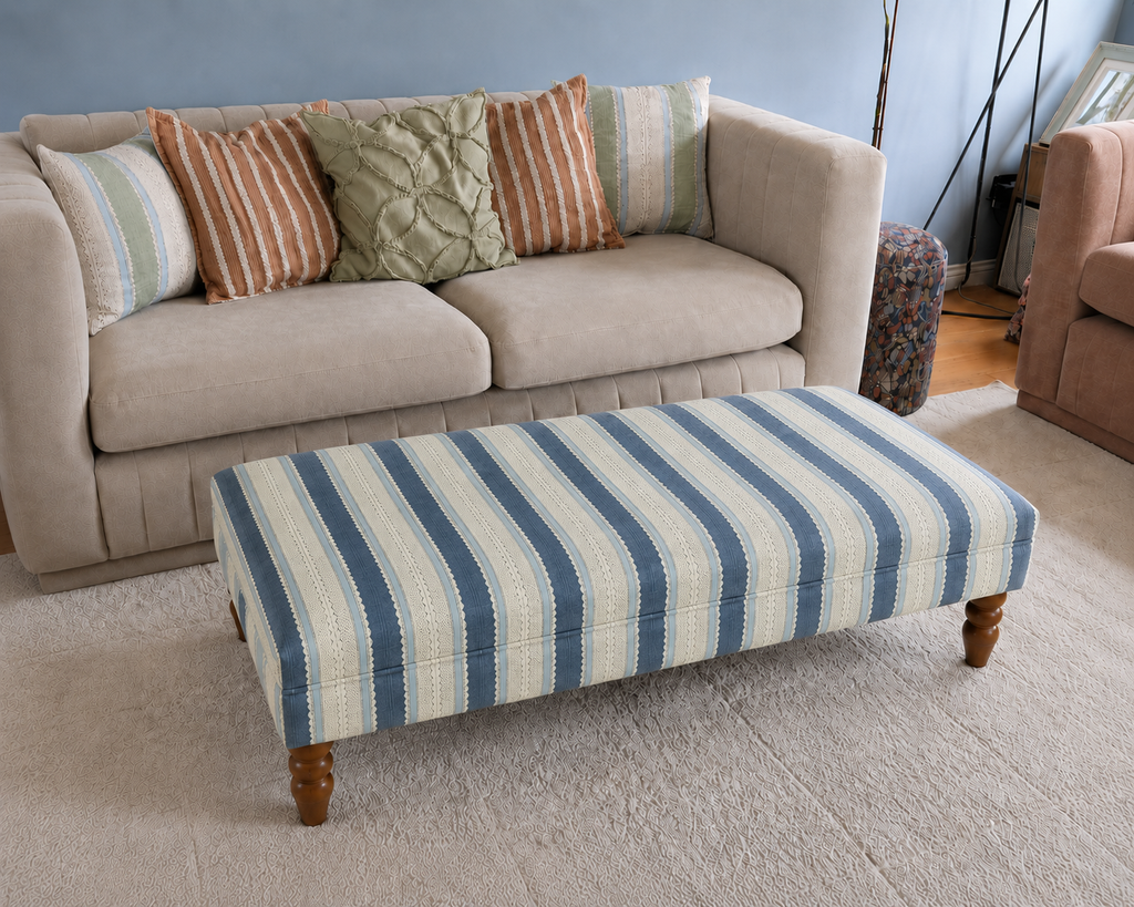 Handmade upholstered footstool in blue and cream Linwood Dimity striped fabric, styled in front of a neutral sofa.