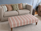 Handmade coffee table footstool upholstered in pink and cream Linwood Dimity fabric with turned wooden legs, styled in a neutral living room.