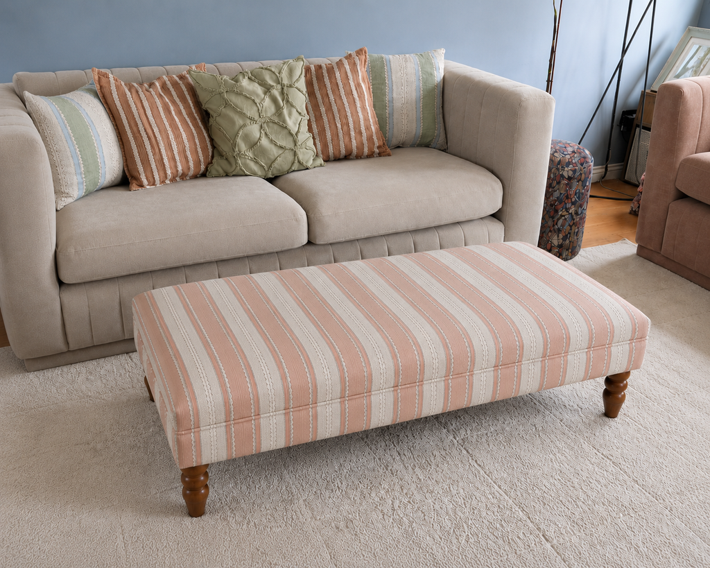 Handmade coffee table footstool upholstered in pink and cream Linwood Dimity fabric with turned wooden legs, styled in a neutral living room.