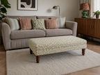 Modern stylish living room with an upholstered footstool in a green and pink botanical abstract swirl pattern on a cream rug.